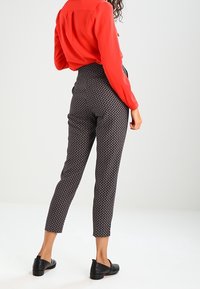 Pantaloni neri a fantasia con vita alta e vestibilità slim, abbinati a una blusa rossa brillante e scarpe basse nere. Tessuto dalla consistenza liscia.