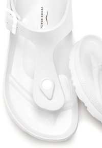 White flip-flop sandals featuring a thong design, adjustable strap, textured footbed, and smooth sole with a circular button detail.