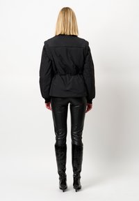 Zwarte pufferjack met een cinched taille, gecombineerd met zwarte leren broek en hoge glanzende haklaarzen. Gladde textuur en minimalistisch ontwerp.