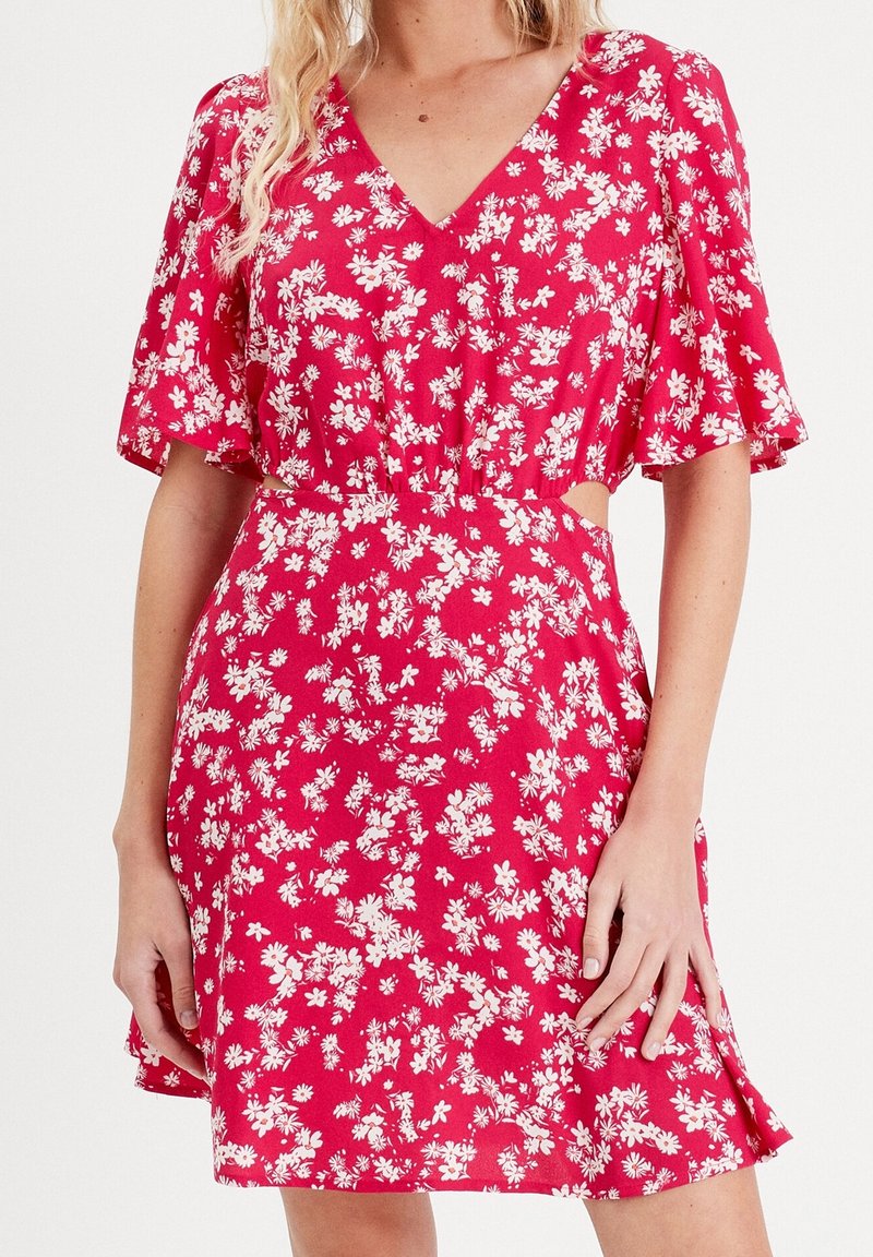 Robe florale rouge avec des manches courtes à volants, décolleté en V, taille cintrée et motifs de fleurs blanches, présentant des découpes sur les côtés.