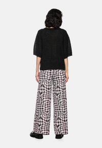 Schwarzes, kurzärmliges Strickoberteil kombiniert mit weit geschnittenen, gemusterten Hosen in weißem, schwarzem und lila Karomuster. Strukturiertes und locker sitzendes Design.