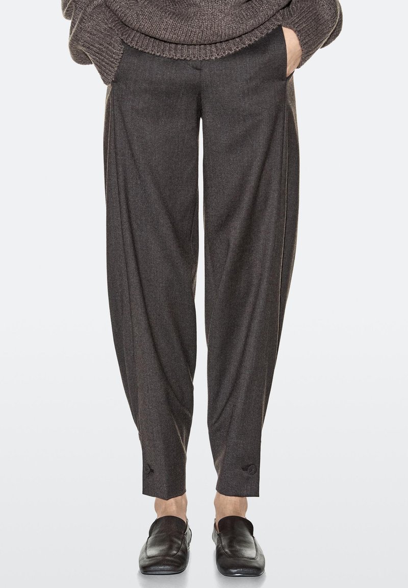 Pantalon gris foncé sur mesure en tissu texturé, avec une coupe ample, des ourlets retroussés et des poches latérales pour un look contemporain.