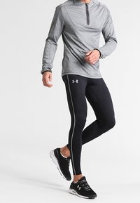 Sudadera atlética de manga larga gris con cremallera combinada con leggings negros ajustados que cuentan con franjas laterales blancas y zapatillas de correr negras.