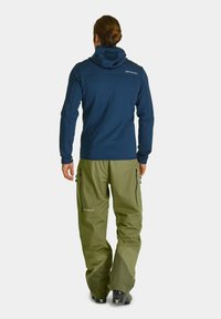 Navy hooded jacket with fitted sleeves, paired with loose-fitting olive green pants featuring zip pockets and reinforced cuffs.
