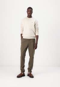 Beige sweatshirt med ribbede mansjetter, sammen med olivengrønne bukser og brune lærersko. Enkelt design uten synlige mønstre eller logoer.