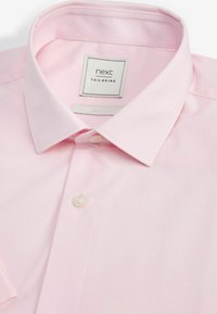 Chemise habillée pour homme de couleur rose clair, avec un col classique, un bouton visible unique, et une étiquette "next tailoring" à l'intérieur du col.