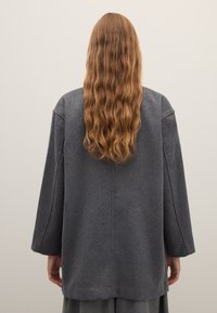 Grauer Wollmischmantel mit entspannter Silhouette, weiten Ärmeln und unstrukturiertem Design. Weiche Textur mit leichtem Glanz.