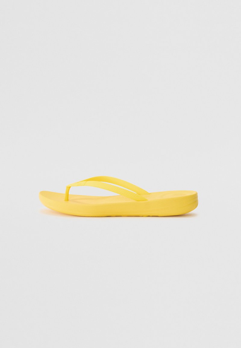 Keltainen flip-flop-sandaali, jossa on litteä pohja, kaksi ohutta hihnaa, sileä pinta ja yksinkertainen muotoilu. Sopii rentoon käyttöön.