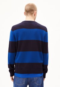 Langärmliger Pullover mit dunkelblauen und marineblauen horizontalen Streifen, Rippkragen und Saum, weicher Textur, getragen über einem blauen Shirt mit runder Saum.
