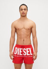 Červené plavky s viazaním v páse a veľkým bielym textom "DIESEL". Vyrobené z ľahkého materiálu, vhodné na vodné aktivity.