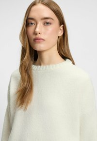 Helle Cremefarbene Sweater mit rundem Halsausschnitt in Rippstrick und weicher Textur, die einen lockeren Schnitt und minimalistische Details bietet.