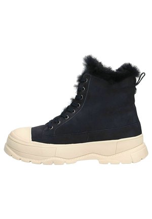 Bottines en daim marine avec bordure en fausse fourrure, capuchon en caoutchouc blanc et semelle épaisse. Présente des œillets en métal et une languette à l'arrière pour un enfilage facile.