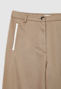 Beige Hosen aus einem strukturierten Stoff, mit einem einzelnen weißen Akzentstreifen in der Nähe der Tasche und einem normalen Knopfverschluss.
