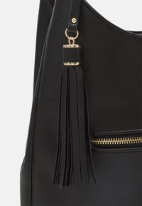 Svart handväska i texturerat läder, med en guldfärgad dragkedja och metallaccenter. Inkluderar en dekorativ svart tofsdetalj.