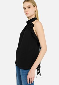 Top nero a collare con dettagli arricciati, realizzato in tessuto leggero e dotato di fessure laterali, abbinato a jeans in denim blu.