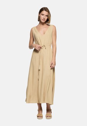 Mujer con un vestido maxi sin mangas color beige, con escote en V y cinturón anudado en la cintura, combinado con sandalias de plataforma trenzadas.