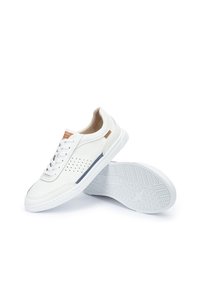 Zapatillas de cuero blancas con diseño perforado y acentos beige, que cuentan con una suela de goma blanca texturizada y un detalle azul en contraste en el lateral.
