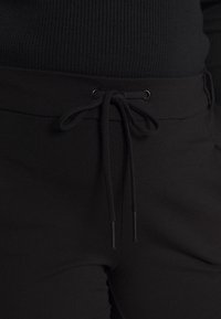 Pantaloni jogger neri con cintura regolabile e aghetti neri, texture liscia e design slim fit. Tessuto morbido per il massimo comfort.