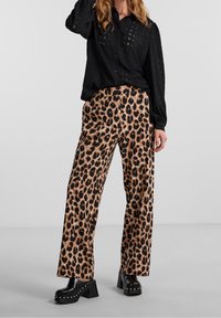 Musta pitkähihainen paita, jossa on silmukkaraitoja, yhdistetty leveälahkeisiin leopardikuosisii housuihin ruskeassa ja mustassa värissä. Paksut mustat platform-kengät.