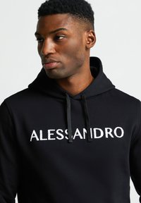 Felpa nera con grafica bianca "ALESSANDRO". Presenta un cappuccio con coulisse e una texture liscia. Design aderente.