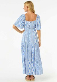 Blauwe en witte geprinte maxi-jurk met een vierkante hals, korte pofmouwen, getailleerde taille en gelaagde rok. Sandalen zichtbaar aan de onderkant.