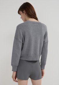 Sweatshirt gris court avec des poignets et un ourlet côtelés, présentant une coupe confortable et une texture douce. Porté avec un short gris assorti.
