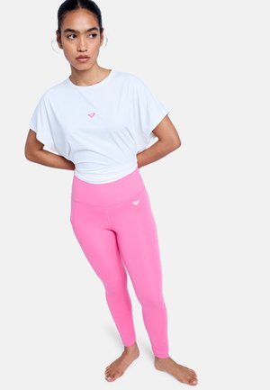 Biały top z krótkim rękawem z małym różowym logo oraz różowe legginsy z wysokim stanem. Gładka tkanina, dopasowany krój, odpowiedni do aktywnego trybu życia.