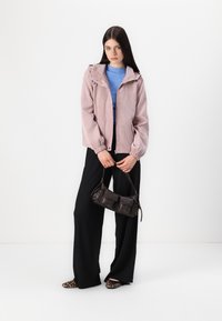 Lyserød kordfløjlsjakke med hætte, blå sweater under, sorte vide bukser og en mørkebrun crossbody taske. Dyrerelaterede sko.