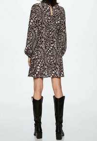 Braun gemustertes Kleid mit einem Schlüsselloch hinten, langen puffigen Ärmeln und einem lässigen Schnitt, kombiniert mit kniehohen schwarzen Stiefeln.