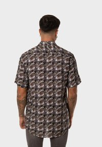 Camisa de manga corta con un patrón de calaveras y follaje en negro, marrón y crema, fabricada en un tejido ligero y con dobladillo recto.
