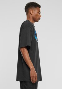 Sort bomulds t-shirt med løs pasform, korte ærmer og et grafisk design med blå accenter på forsiden. Enkel rund hals.