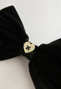 Fascia in velluto nero con una finitura texturizzata, caratterizzata da un accento a forma di cuore in oro con la scritta "BAKER" incisa.