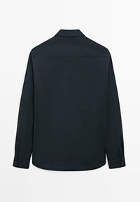 Chemise sombre à manches longues vue de dos avec col et poignets boutonnés à chaque manche sur un fond uni.