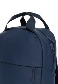 Granatowy plecak o gładkiej, matowej powierzchni. Posiada regulowane szelki, uchwyt na górze oraz zasuwaną kieszeń z przodu.