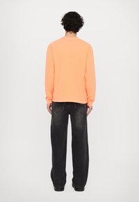 Langærmet, klar orange skjorte lavet af bomuld, parret med løse, mørke denim jeans. Vist fra bagsiden.