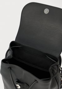 Juodos spalvos odinė kuprinė su viršutiniu atidarytu dangteliu, matoma erdvi vidinė dalis ir raišteliu užsegamas uždarymas, ant šviesaus fono.