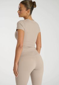 Beige, figursydd träningstopp med korta ärmar, matchad med högmidjade leggings. Slät textur och minimal branding synlig.