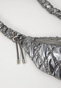 Marsupio imbottito di colore argento metallizzato con cerniera e tracolla regolabile su uno sfondo bianco.