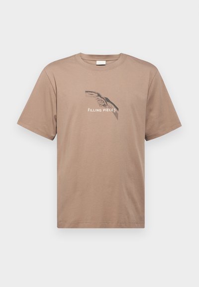 Beige Baumwoll-T-Shirt mit kurzen Ärmeln und Rundhalsausschnitt, das ein grafisches Design von Händen und den Text "FILLING PIECES" darunter zeigt.