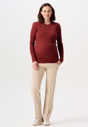 Bordeauxfarbener, gerippter Pullover mit langen Ärmeln, kombiniert mit beigen, maßgeschneiderten Hosen und hellen Sneakers. Glatte Textur und taillierter Schnitt.