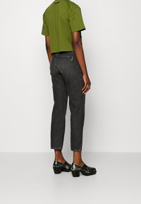 Crops green cotton t-shirt, dark denim jeans with back pockets, and glossy black platform shoes with metallic accents.
