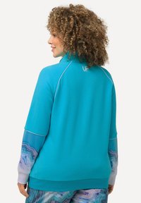 Sudadera de forro polar turquesa con mangas largas. Presenta detalles en blanco y un patrón marble azul único en las mangas. Logo en la parte posterior del cuello.