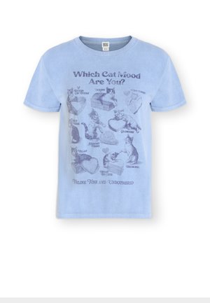 Lyseblå T-shirt med trykte katte i forskellige positurer, mærket med stemninger som "Joules," "Glamcore" og "Skurk" under teksten "Hvilket Kattehumør Er Du?"