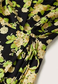Tissu de robe florale noire avec de grandes fleurs crème et vertes, avec des détails froncés et un lien, texture lisse.