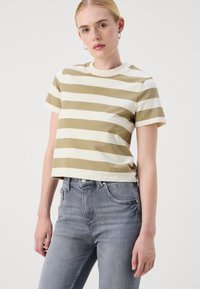 Κοντομάνικο, κομμένο μπλουζάκι σε ελαιόλαδο και κρεμ οριζόντιες ρίγες, φτιαγμένο από βαμβάκι; συνδυασμένο με ψηλόμεσα, ανοιχτό γκρι τζιν.