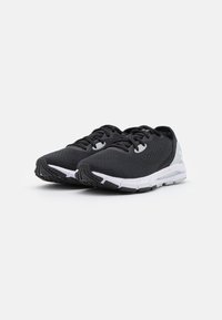 Baskets de sport noires avec tige en mesh, bout rond, semelle blanche, grip texturé et lacets. Présente un logo au talon et des accents sur les côtés.