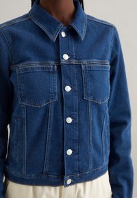 Denim jasje in donkerblauw met een klassiek kraag, twee voorkwesten, zilveren knoopsluitingen en contrasterende stiksels.