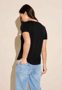 Černé tričko s krátkým rukávem a kulatým výstřihem, nošené s světle modrými denimy. Hladká textura, jednoduchý design.