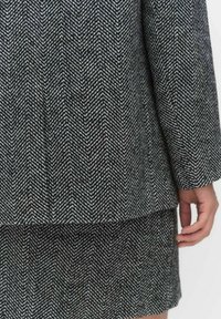 Kaksiosainen houndstooth-asukokonaisuus mustavalkoisena, jossa on rakenteellinen takki ja hame, jotka on valmistettu teksturoidusta kankaasta ja joissa on selkeä kuvio.