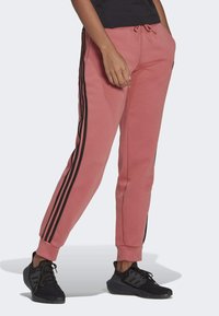 Roze sweatpants met een aansluitende pasvorm, zwarte zijstrepen, elastische boorden en een trekkoord in de taille. Gepaard met zwarte sportschoenen.